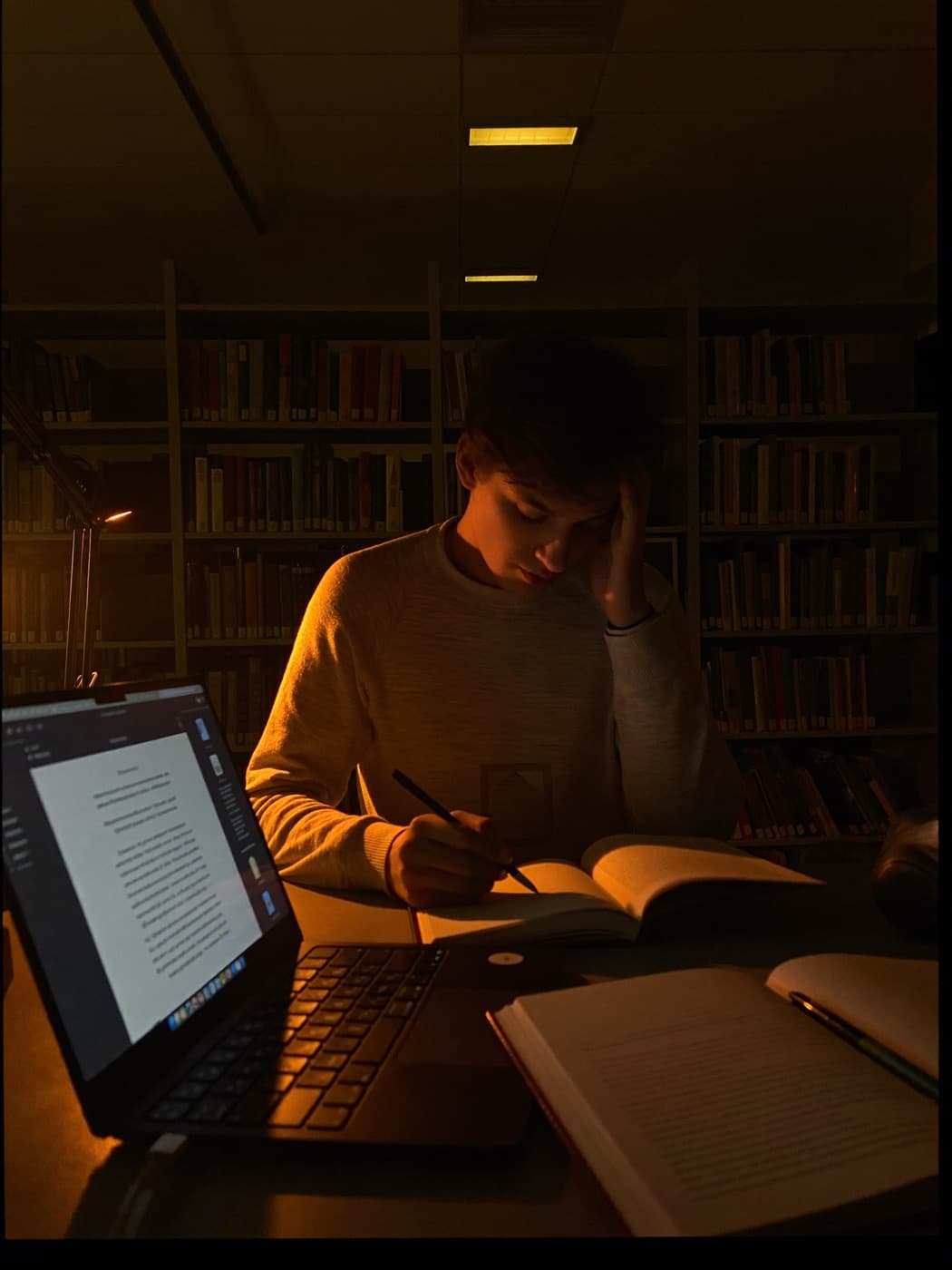 Student studying late in a dark library under a warm desk lamp