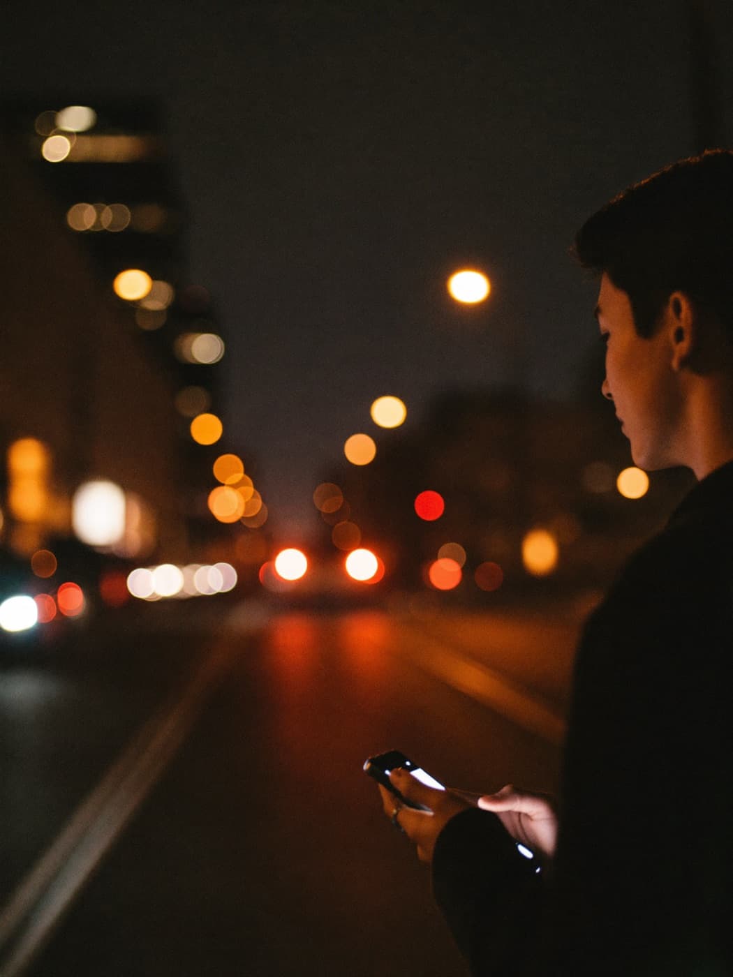 Person walking through a city street at night holding a phone